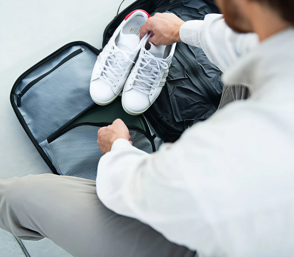 Homme rangeant ses chaussures dans sa valise qui comporte un sac compressé Skood.